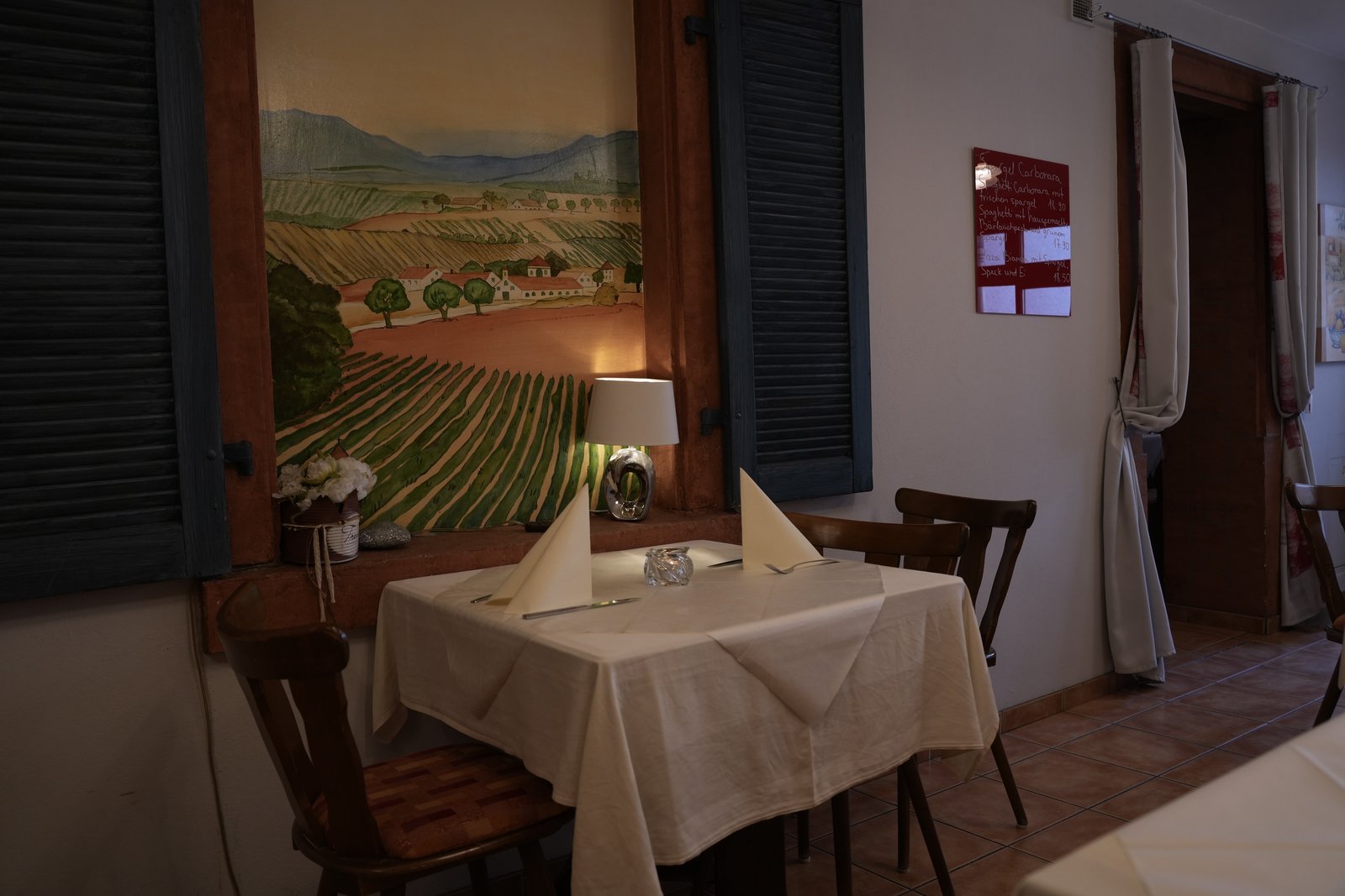 Gedeckter Tisch mit weißer Tischdecke vor einem Weinberg-Wandbild